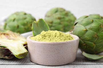 Bowl with powder and fresh artichokes on white wooden table, closeup