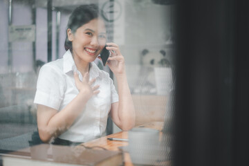 Fototapeta premium Attractive young woman looking camera and talking on the mobile phone and smiling while sitting at her working place in office and looking at laptop