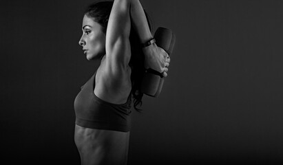 Muscular woman doing stretching and strength workout on the shoulders, blades and arms in holding dumbbells back behind herself on black background with empty space. Profile view. - 624978301