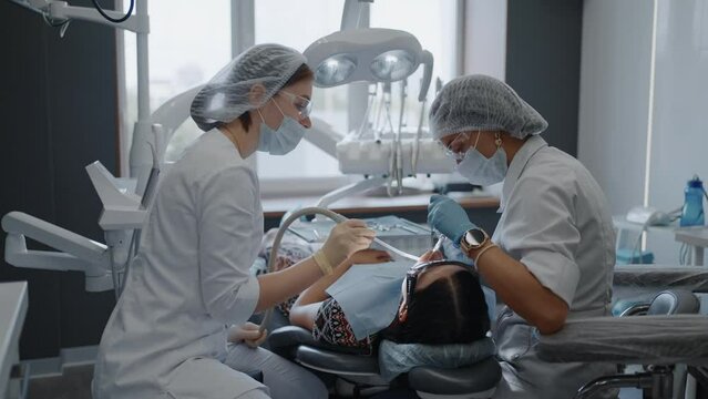 Professional Dentist And Assistant Curing Teeth Of Patient In Contemporary Office Of Dental Clinic