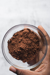 Cocoa powder in a glass bowl, clumpy cocoa powder into a small transparent bowl
