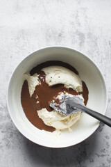 Chocolate cake batter being mixed in a white bowl, folding cake batter in a white mixing bowl, the process of making chocolate cake