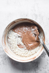 Chocolate cake batter being mixed in a white bowl, folding cake batter in a white mixing bowl, the process of making chocolate cake
