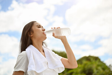 A healthy Asian woman is drinking water from a bottle, feeling thirsty, resting after a long run
