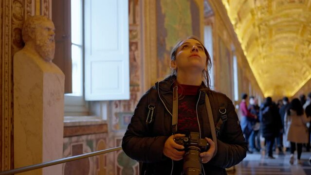 Contemplating Hispanic young woman in black jacket standing while walking in the Gallery pf Maps, golden corridor adorned by rescoes of maps in Vatican museum in Rome, Italy