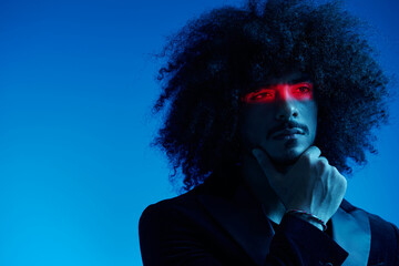 Fashion portrait of a man with curly hair on a blue background with a red stripe of light, multicolored light, trendy, modern concept.