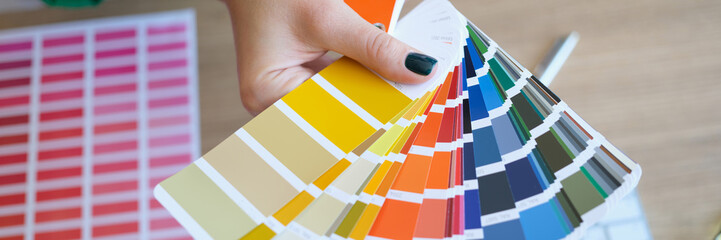 Woman's hand holds color swatches over her desk.