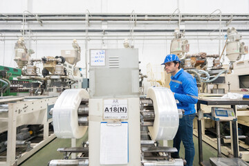 American male engineer, mechanic supervisor Stand and watch the production of the goods of the machine in action. Wear a helmet and uniform. In the plastic and steel industry