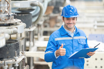American male engineer, mechanic supervisor Thumbs up like and smiling holding radio and list note. There are machines working around. Wear a helmet and uniform. In the plastic and steel industry