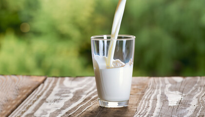 milk pouring into glass on wooden table outdoors