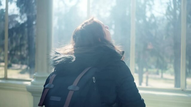 Pensive young Latin woman tourist in warm clothes with professional photo camera walking through the mist and the rays of light and standing inside of The Glass Palace in Madrid, Spain 