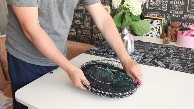 A man is unpacking a parcel. Top trap for crayfish and fish. Lays a trap on the table.