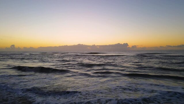 Drone shot flying low over a beach and low over waves towards the ocean during sunrise in Caril&oacute;, Argentina.