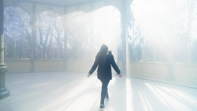 Happy young Latin woman tourist in warm clothes with professional photo camera walking through the mist and the rays of light and standing inside of The Glass Palace in Madrid, Spain 