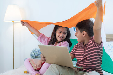Happy excited Indian boy and girl waving Indian flag on head and  laptop computer on boy's lap