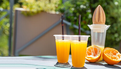 disposable plastic glass of cold freshly squeezed orange juice with wooden juicer on table outdoors. Fresh drink concept