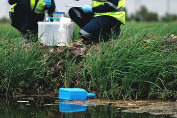Chemical Tanks, Toxic Waste or Suspicious Pollutants Float on the Rotten Smelly Pond Water Sources Surface with Environmental Engineers Monitoring the Water Quality in the Background.
