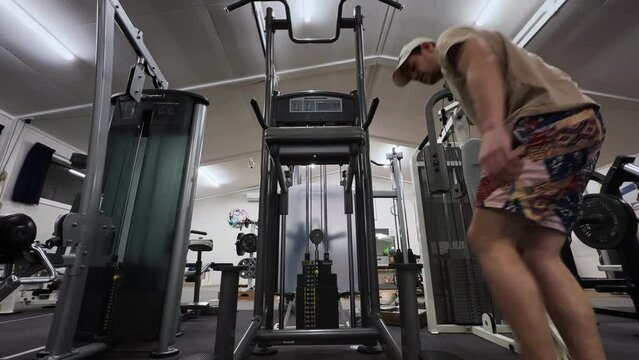skinny, young man doing dips inside gym; static view from behind