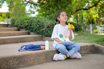 Little kid girl asian holding and eat banana in the school. feel happy and enjoy eating banana  before entering the classroom.