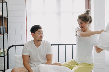 Fototapeta premium Asian wife and husband playing pillow fight funny and laugh on the bed.