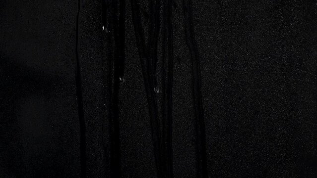 Many water drops running down a plane surface with a black background
