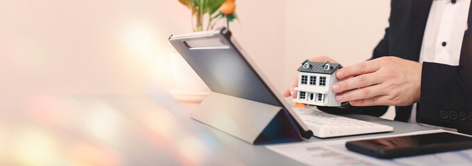 Real estate agent holding house model in front of laptop. Real estate business concept.