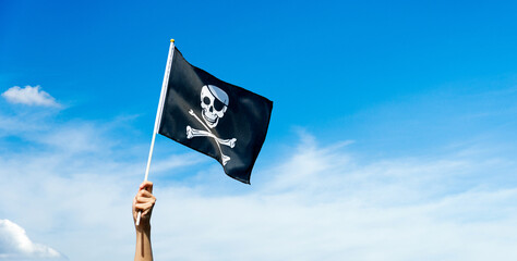 Skull flag in hand waving against blue sky background