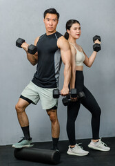 Fototapeta na wymiar Portrait studio shot of strong fit young male and female muscular fitness model in sleeveless shirt sport bra and legging standing posing lifting weight metal dumbbells showing biceps together in gym