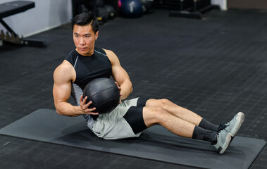 Fototapeta na wymiar Millennial Asian strong young fit male muscular fitness model in sportswear sleeveless shirt and sporty shorts laying down sit up, holding heavy leather ball workout on floor exercise training in gym
