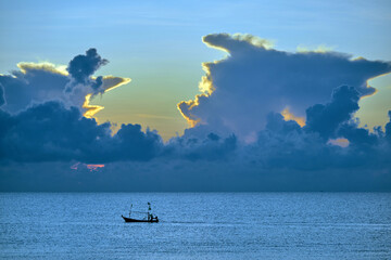 morning sunshine with the cloudy sky over the sea with small silhouette fishing boat below