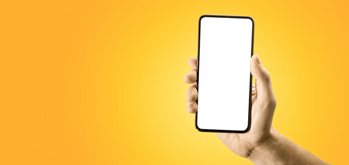 Hand holding black cellphone with blank screen and modern frame less design on yellow background....