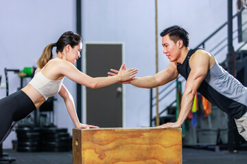 Millennial Asian fit strong muscular male and female fitness model athlete friend couple in sportswear working out training exercising planking together on wooden box ready to do pushing up in gym