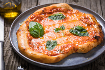 Homemade rustic pizza, prepared on traditional way. Classic Italian Margherita with Mozzarella cheese, tomato sauce and basil leaves on top. Garnished with olive oil