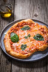 Homemade rustic pizza, prepared on traditional way. Classic Italian Margherita with Mozzarella cheese, tomato sauce and basil leaves on top. Garnished with olive oil