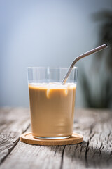 Ice coffee in transparent glass with straw, placed on rustic board. Popular summer coffee cocktail drink.