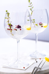 Gin and tonic cocktail with red pepper, lemon and rose buds in gin glasses, in white and bright environment. Perfect summer cocktail drink. 