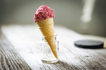 Strawberry Ice cream in cone placed in glass jar with fruit and scoop in rustic scene. Italian gelato.
