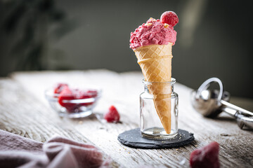 Strawberry Ice cream in cone placed in glass jar with fruit and scoop in rustic scene. Italian gelato.