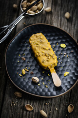 Pistachio ice cream bar on stick, with whole nuts. Italian gelato placed in dark and moody scene on wooden table