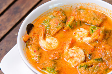 Spicy tamarind soup with veggies and shrimp on the wooden background.