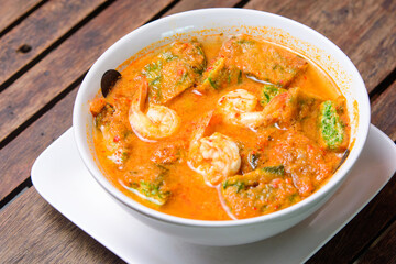 Spicy tamarind soup with veggies and shrimp on the wooden background.