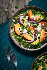 Salad with peach, onion, avocado, nuts and cheese, served on a plate in dark ambient. Healthy super food meal on wooden board.