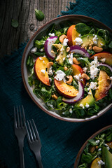 Salad with peach, onion, avocado, nuts and cheese, served on a plate in dark ambient. Healthy super food meal on wooden board.