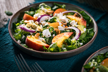 Salad with peach, onion, avocado, nuts and cheese, served on a plate in dark ambient. Healthy super food meal on wooden board.