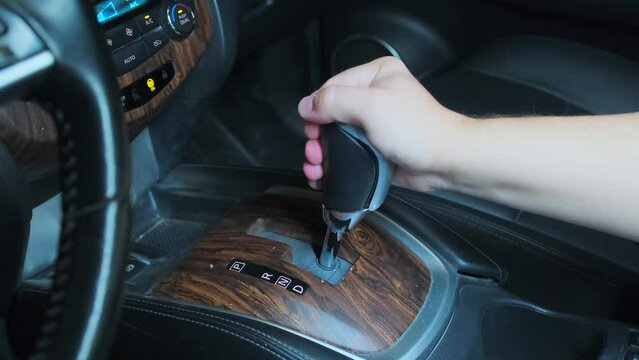 Male hand shifts gears, leather wood-covered car interior. Automatic transmission, automatic gear shift, is moved from P (Park) to D (Drive), side view.