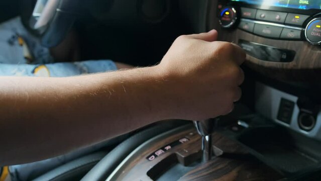 Male hand shifts gears, side view, leather wood-covered car interior. Automatic transmission, automatic gear shift, is moved from P (parking) to D (drive) and back.
