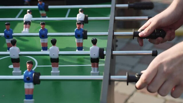 Man twists handles of axes with figurines of football players of board game kicker with his hands in open air. Family entertainment that trains dexterity and attention and develops motor skills.