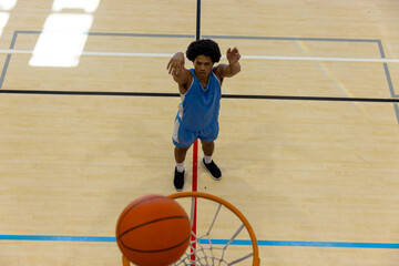Naklejka premium Biracial male basketball player wearing blue sports clothes and shooting basketball at gym
