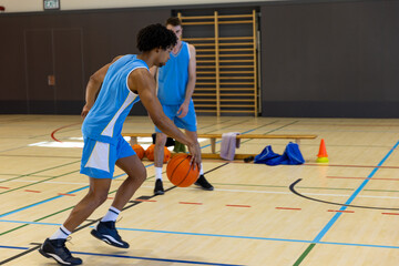 Diverse male basketball players wearing blue sports clothes and playing basketball at gym