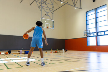 Biracial male basketball player wearing blue sports clothes and shooting basketball at gym